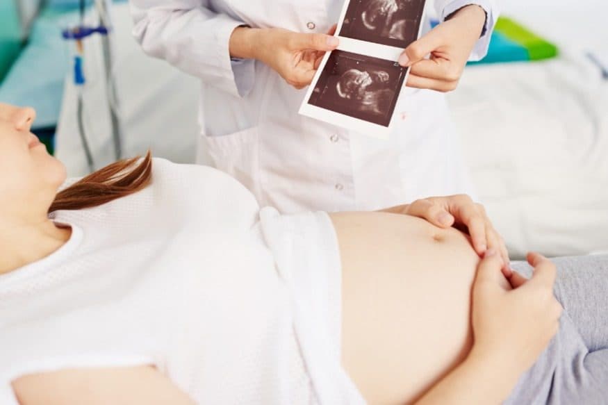 Pregnant woman on an examination bed while a clinician holds up a strip of ultrasound prints